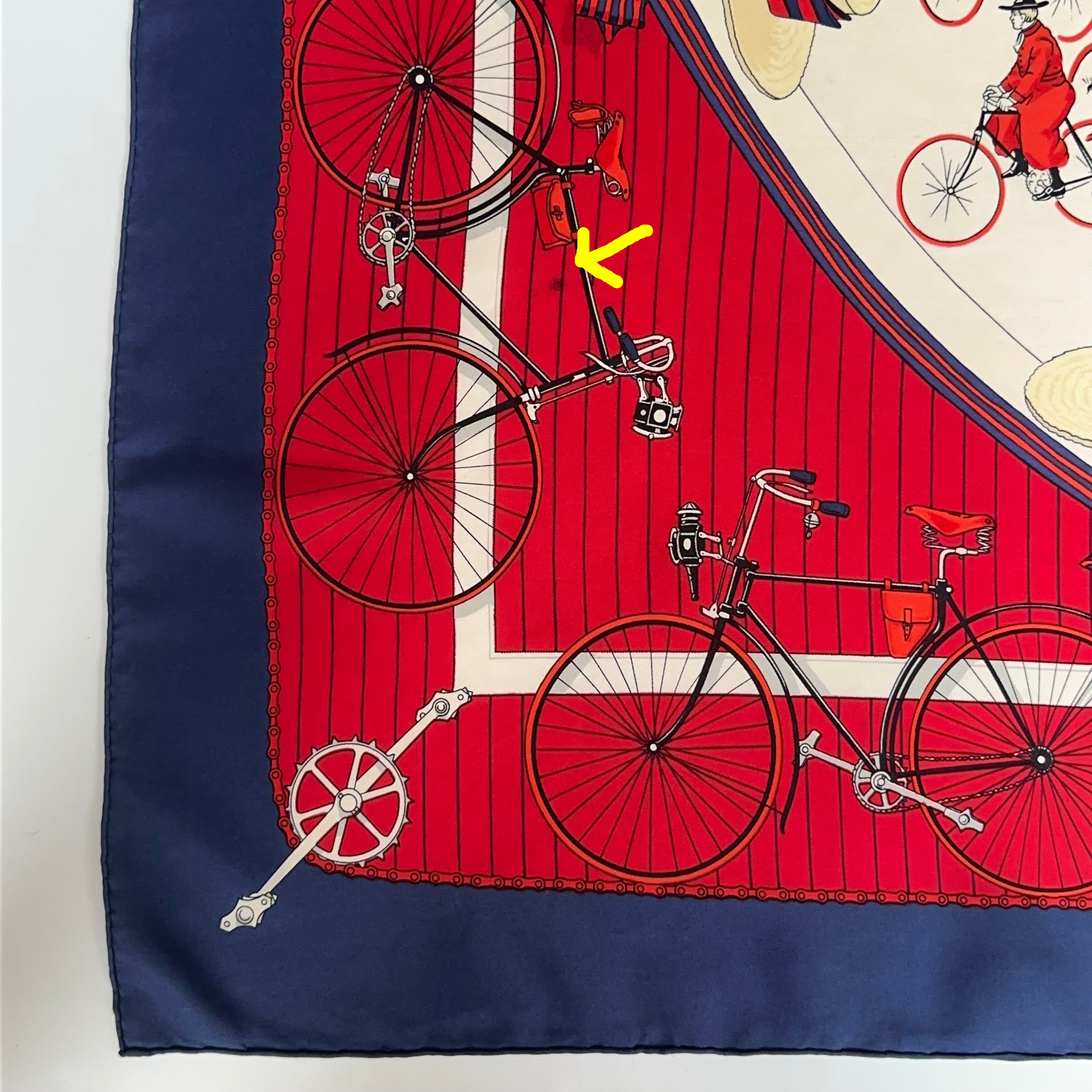 Gros plan sur un angle du carré : motif technique de chaînes, pignons et roues de vélo sur fond rouge rayé.