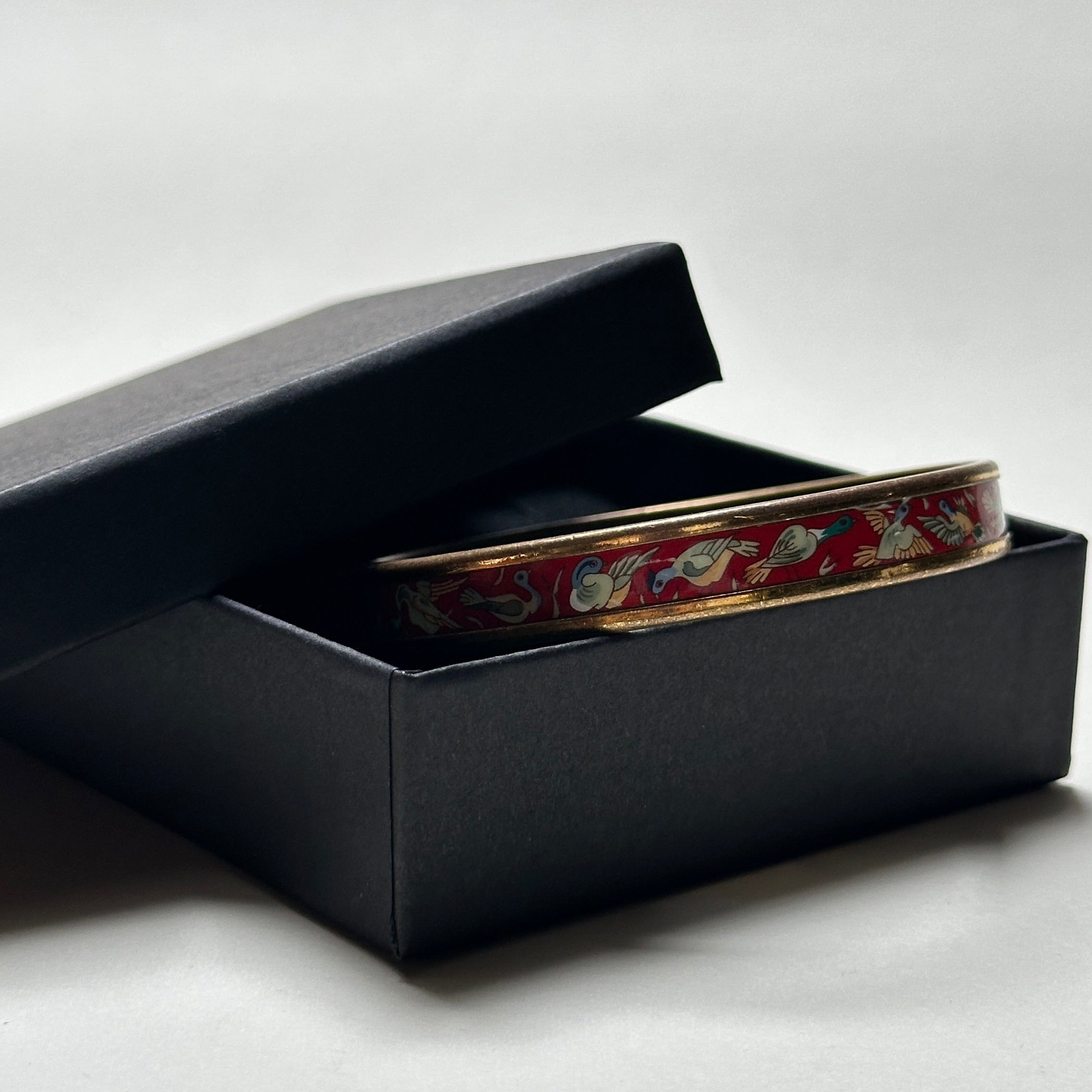 Bracelet jonc Hermès vintage en émail rouge grenat avec motif d'oiseaux migrateurs et finition plaqué or, présenté dans un écrin.